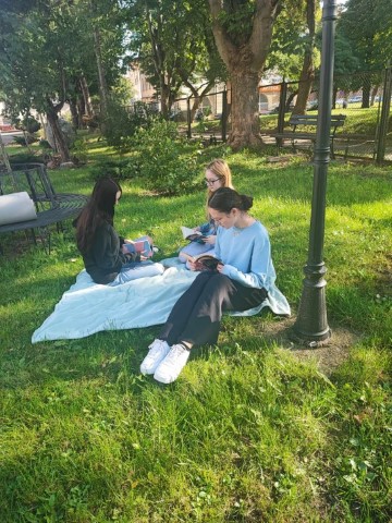trzy dziewczyny siedzą w parku na kocu i czytają książki